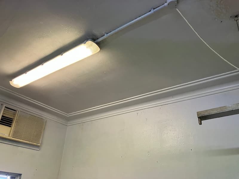 Fluorescent light fixture on a ceiling with air conditioner unit in a room with white walls.
