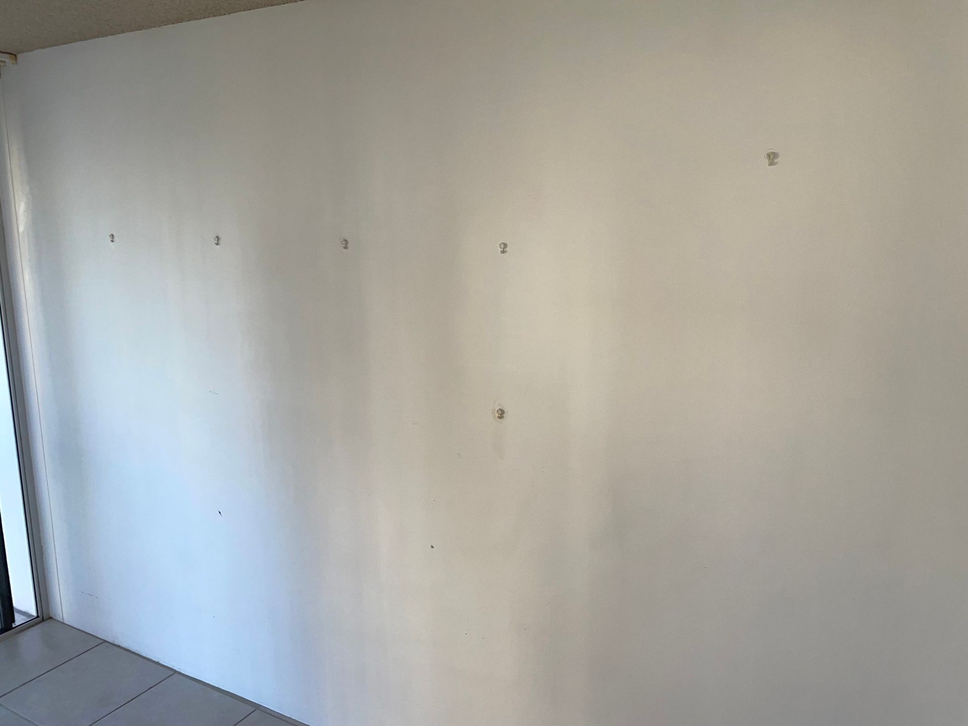 White wall with several small holes, likely from previous hanging items, in an interior setting.
