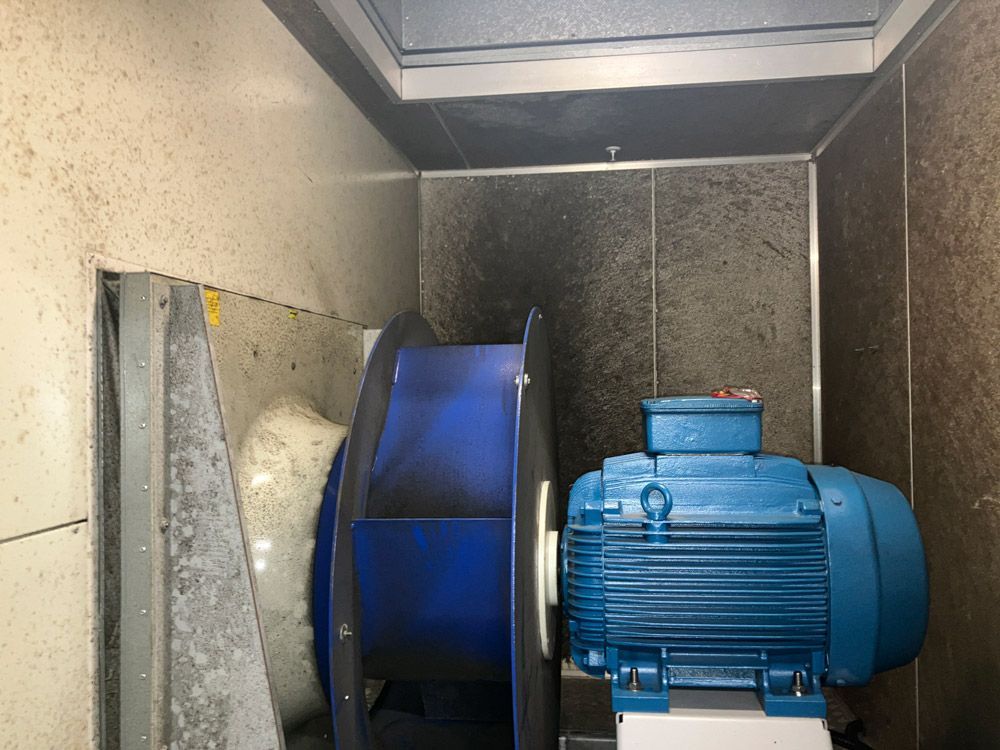 Blue motor and fan inside a ventilation duct, dark walls.