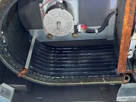 Indoor air handler coil and fan assembly. Black coils, silver fan, and electrical components.