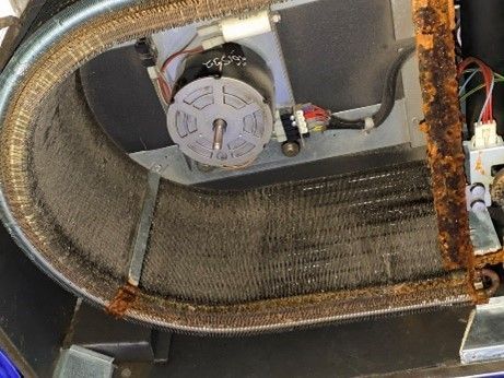 Inside view of a rusted HVAC unit coil and fan motor, in a dark setting.