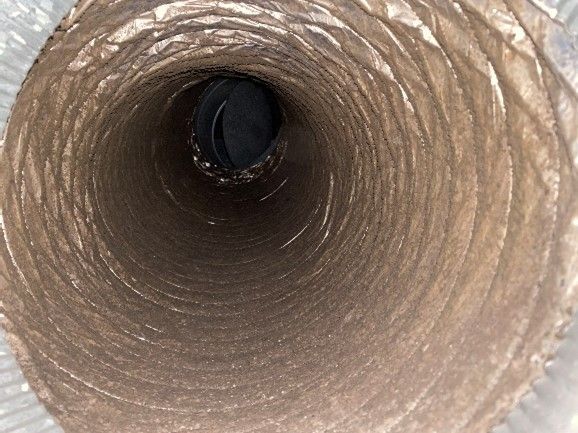 Inside view of a dusty, silver flexible duct. The duct is spiraled, with a dark, obscured opening.