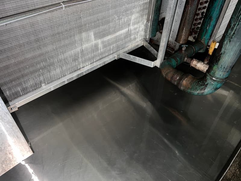 Close-up of a metal surface beneath an air conditioning unit; includes copper pipes and metallic fins.