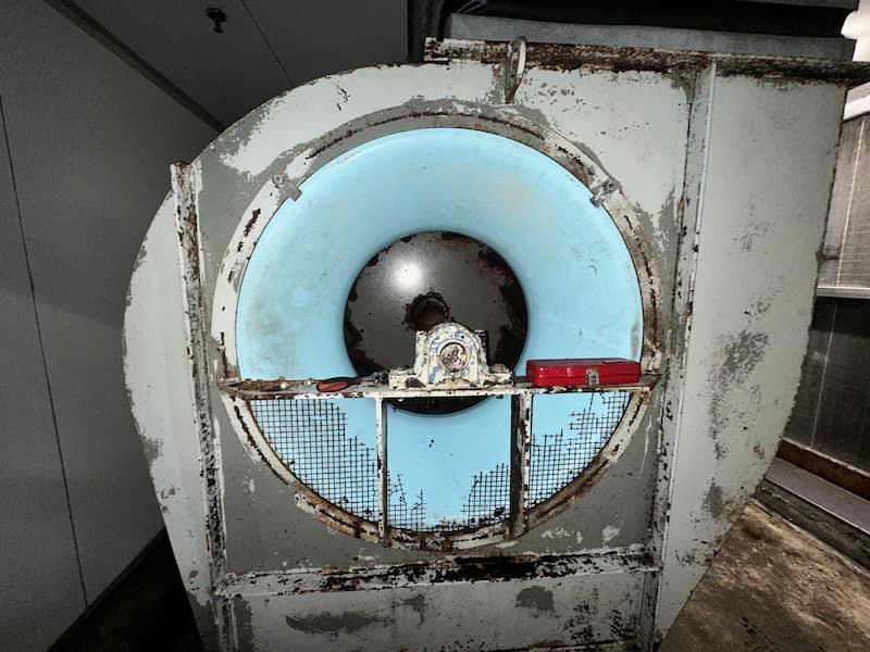 A large, industrial fan with a blue interior, rusty metal, and a protective grate.