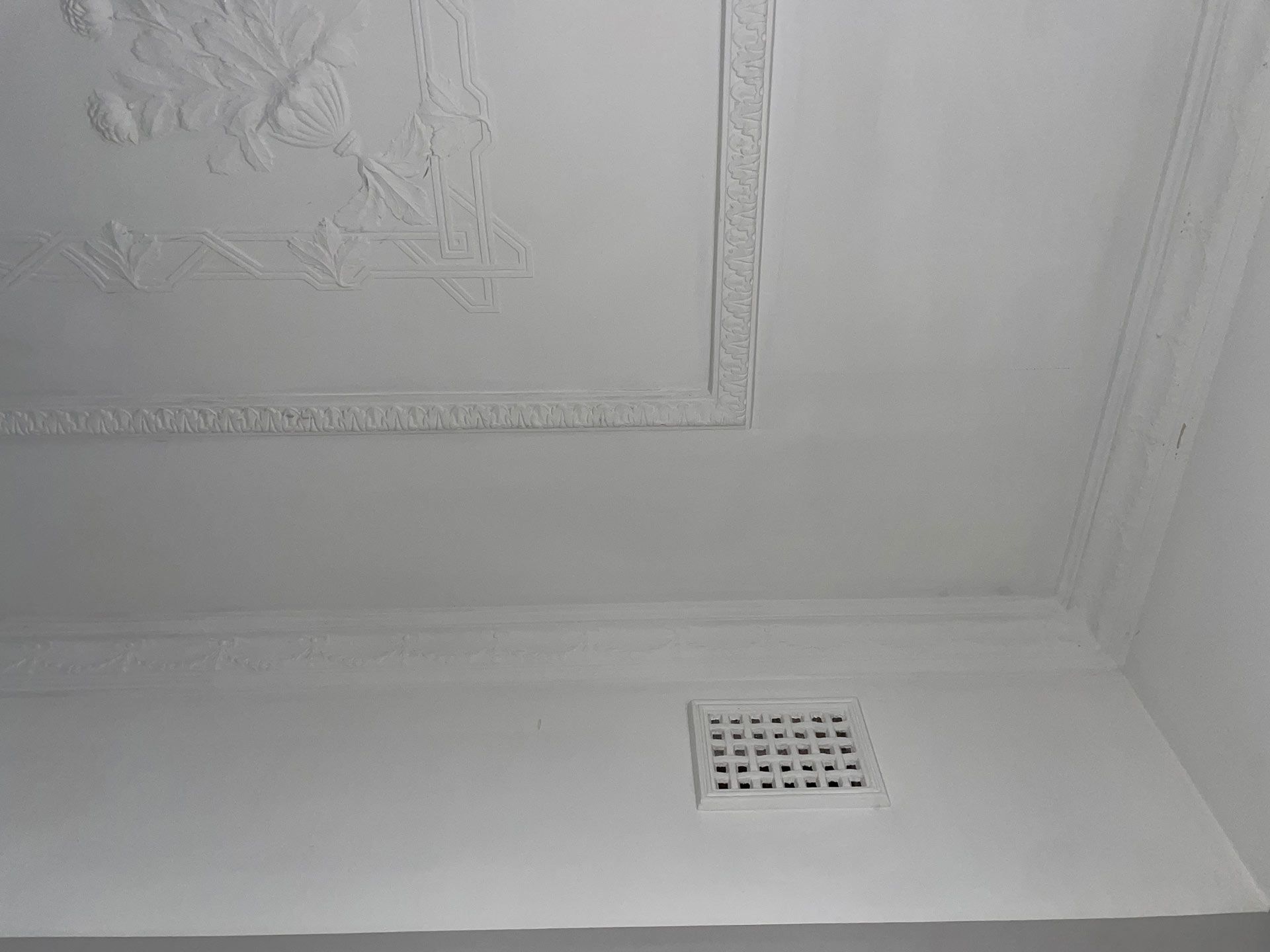 White ceiling with decorative molding, vent, and ornate plaster detailing.
