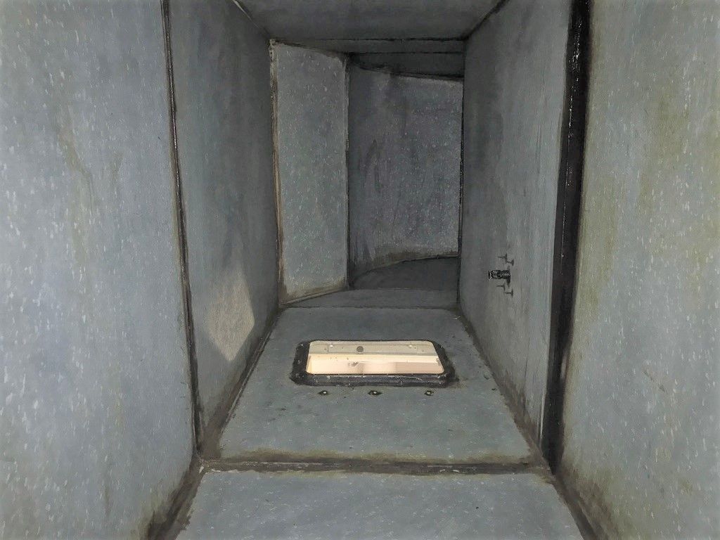 Interior of a rectangular duct, gray walls with a rectangular access panel in the floor.
