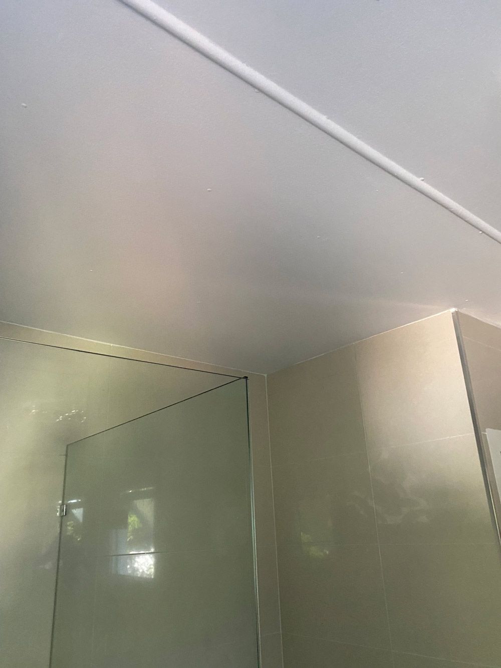 White bathroom ceiling with a white trim and a glass shower wall.