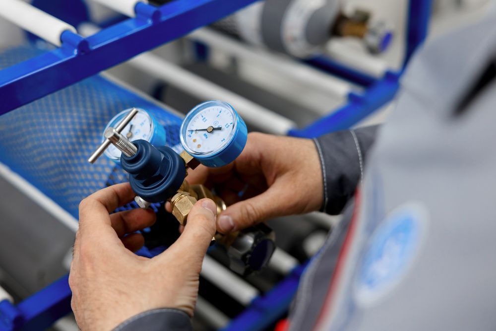 Person attaching a blue pressure gauge to a brass fitting on a gas cylinder.