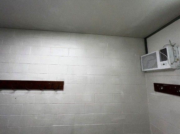 White-painted cinder block walls and ceiling in a room with a mounted air conditioner and a wooden coat rack.