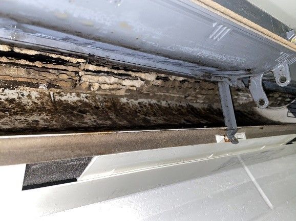 Close-up view of a dirty, moldy air conditioning unit, showing black and brown discoloration.