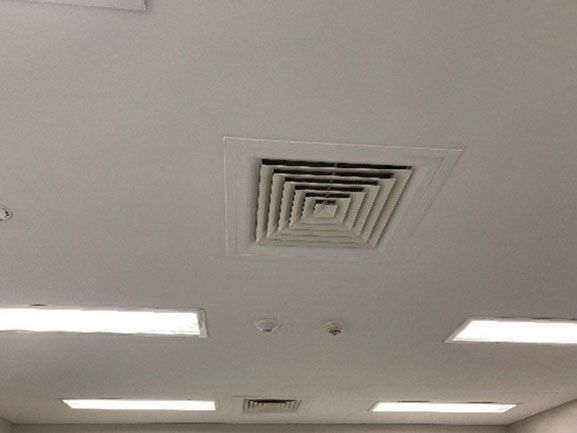 White ceiling with a square air vent and rectangular lights.