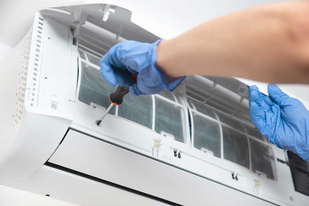 Person in blue gloves using a screwdriver on an air conditioning unit.