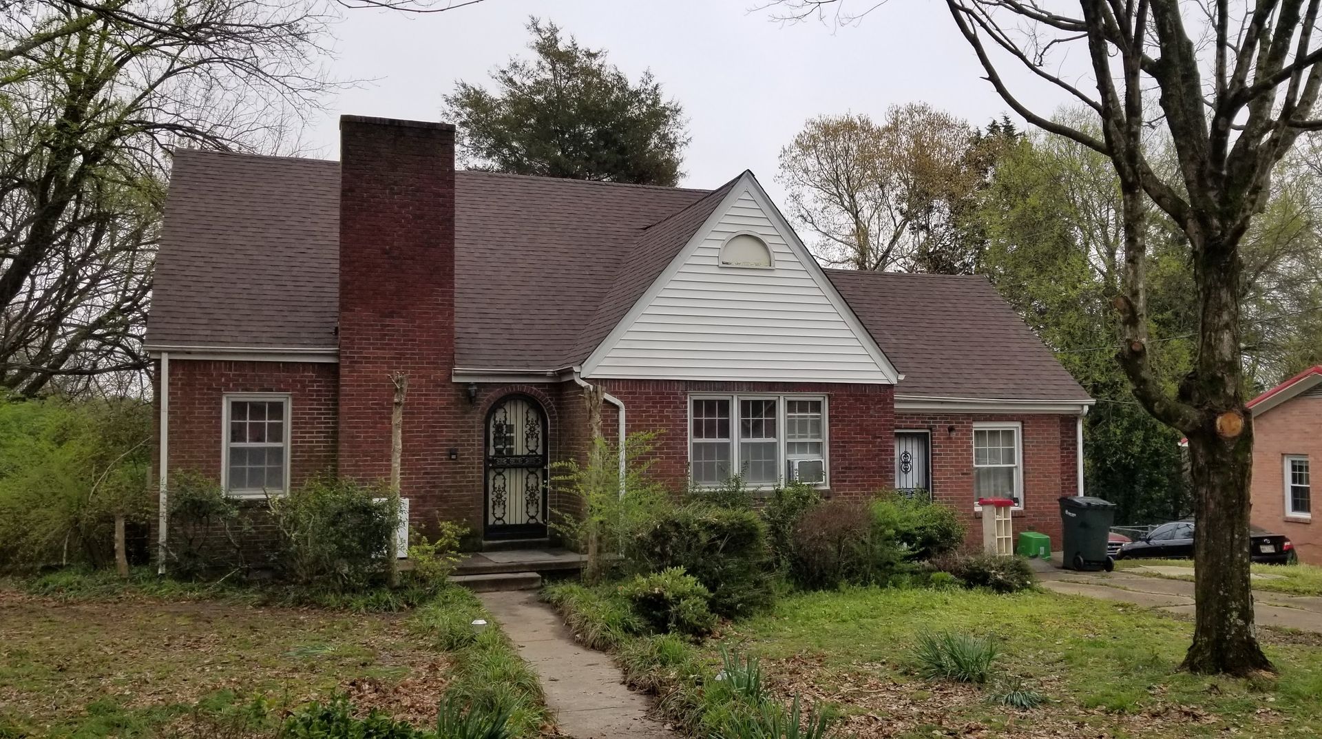 Red brick house with a chimney, small front yard, cloudy day.