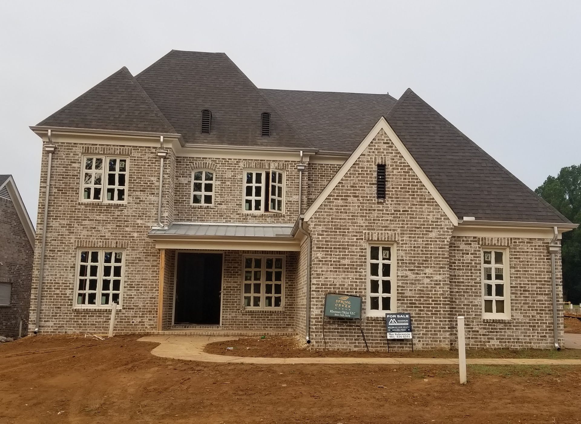 Two-story house under construction with brick facade, windows, and dark gray roof.