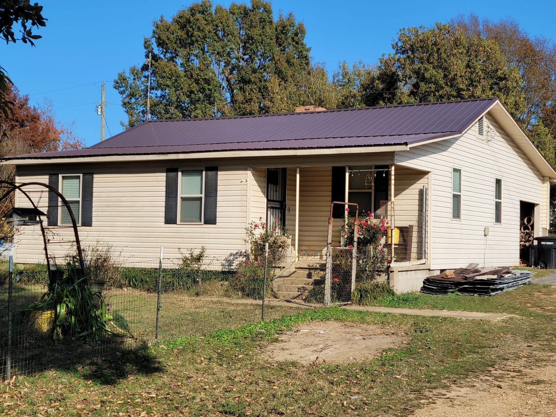 Beige house with brown metal roof, porch, and small yard.