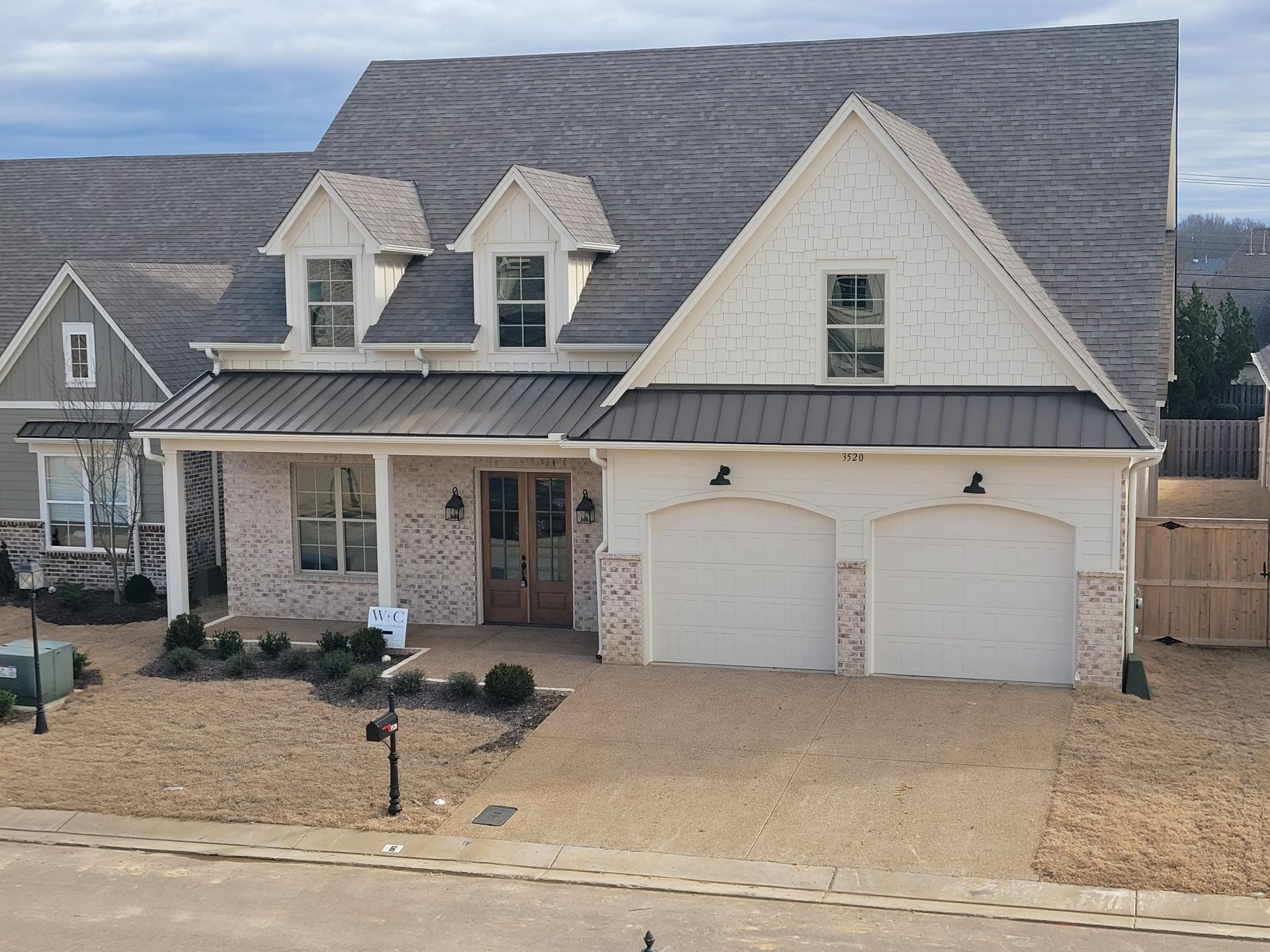 Cream-colored house with a metal roof, brick accents, and two-car garage, set in a gravel yard.