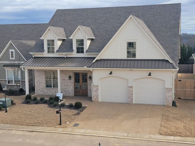 Two-story house with white brick and gray roof. Front porch, two-car garage, and dormers.