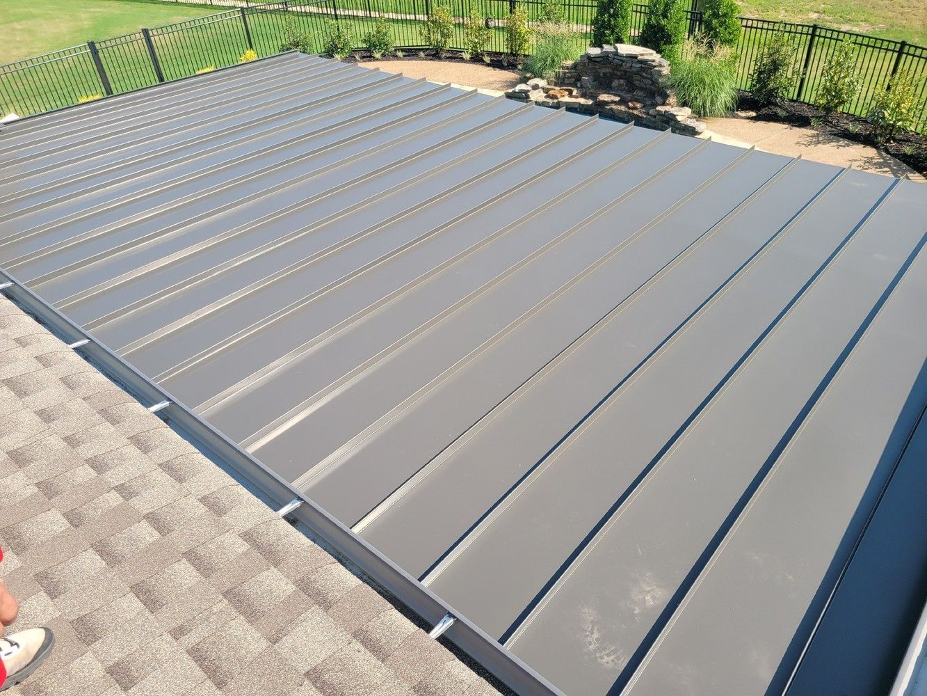 Gray metal roof panels with grooves, next to a brown shingled roof section.