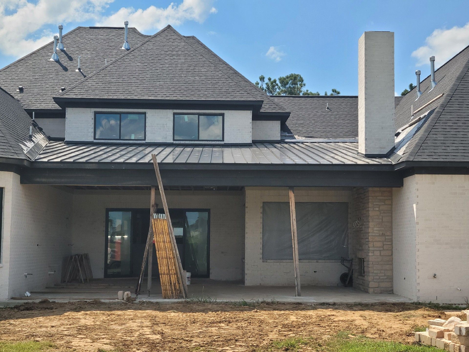 Back of a new house under construction; gray roof, white brick, chimney, and dirt yard.