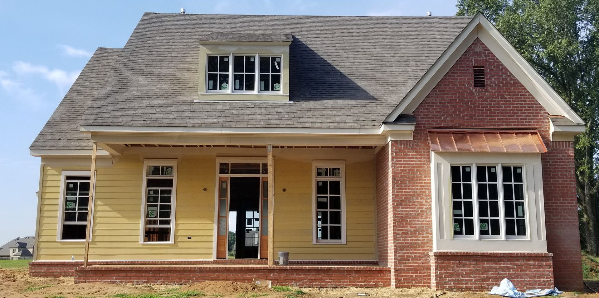 A house under construction; yellow siding, red brick accents, and gray roof.