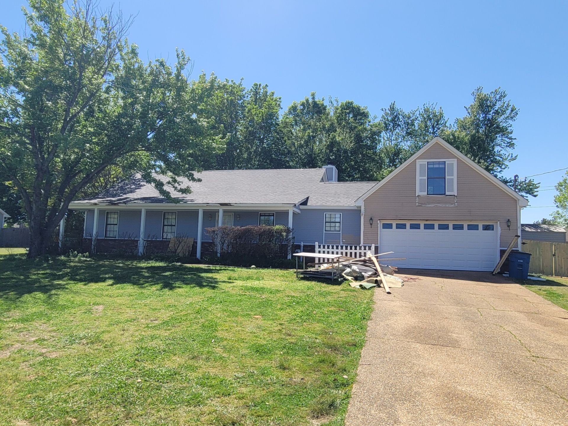 A light blue house with a gray roof, a ramp and a driveway. The sky is blue and the grass is green.