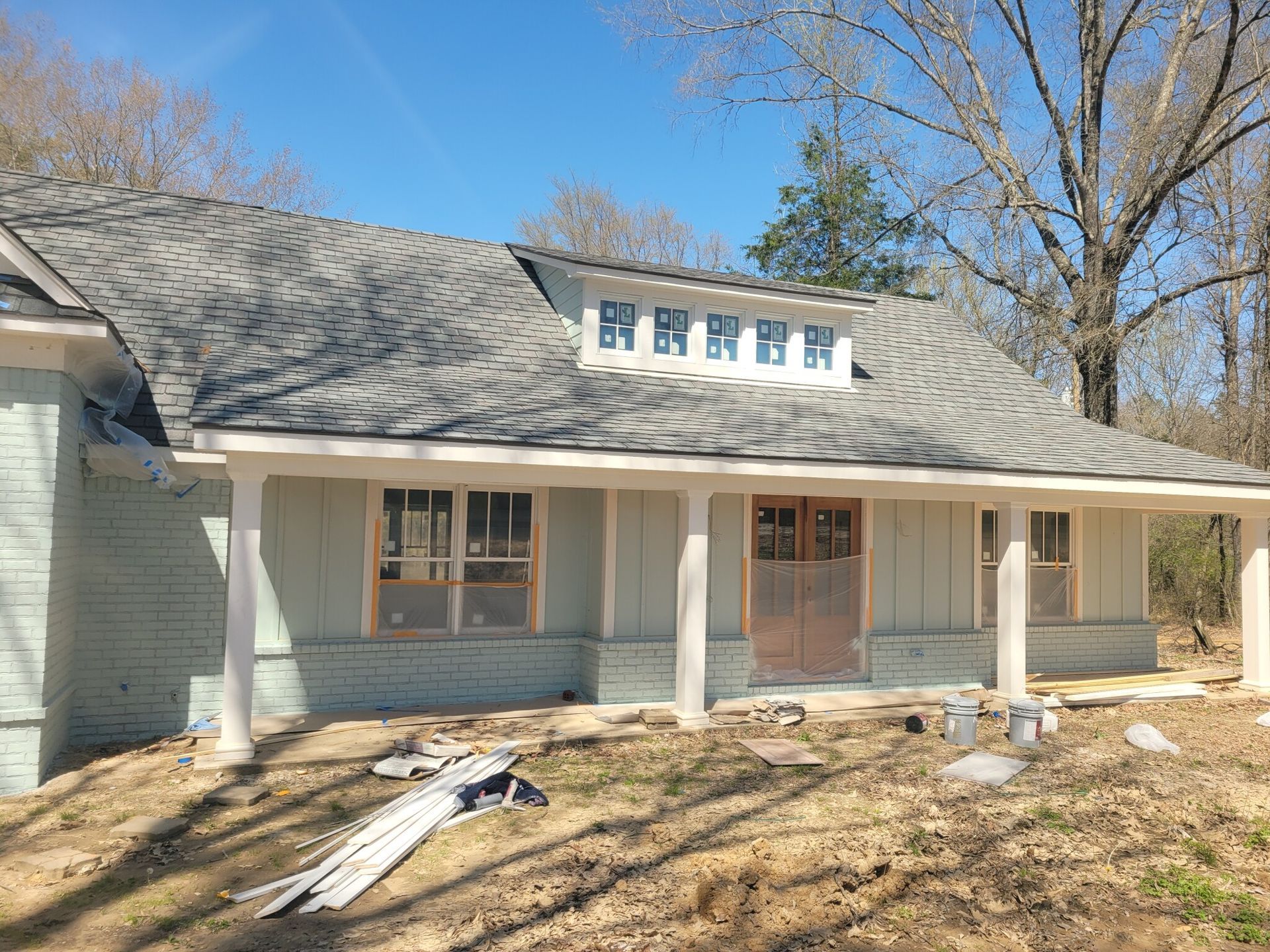Light blue house under construction; porch, roof, windows, and materials on the ground.
