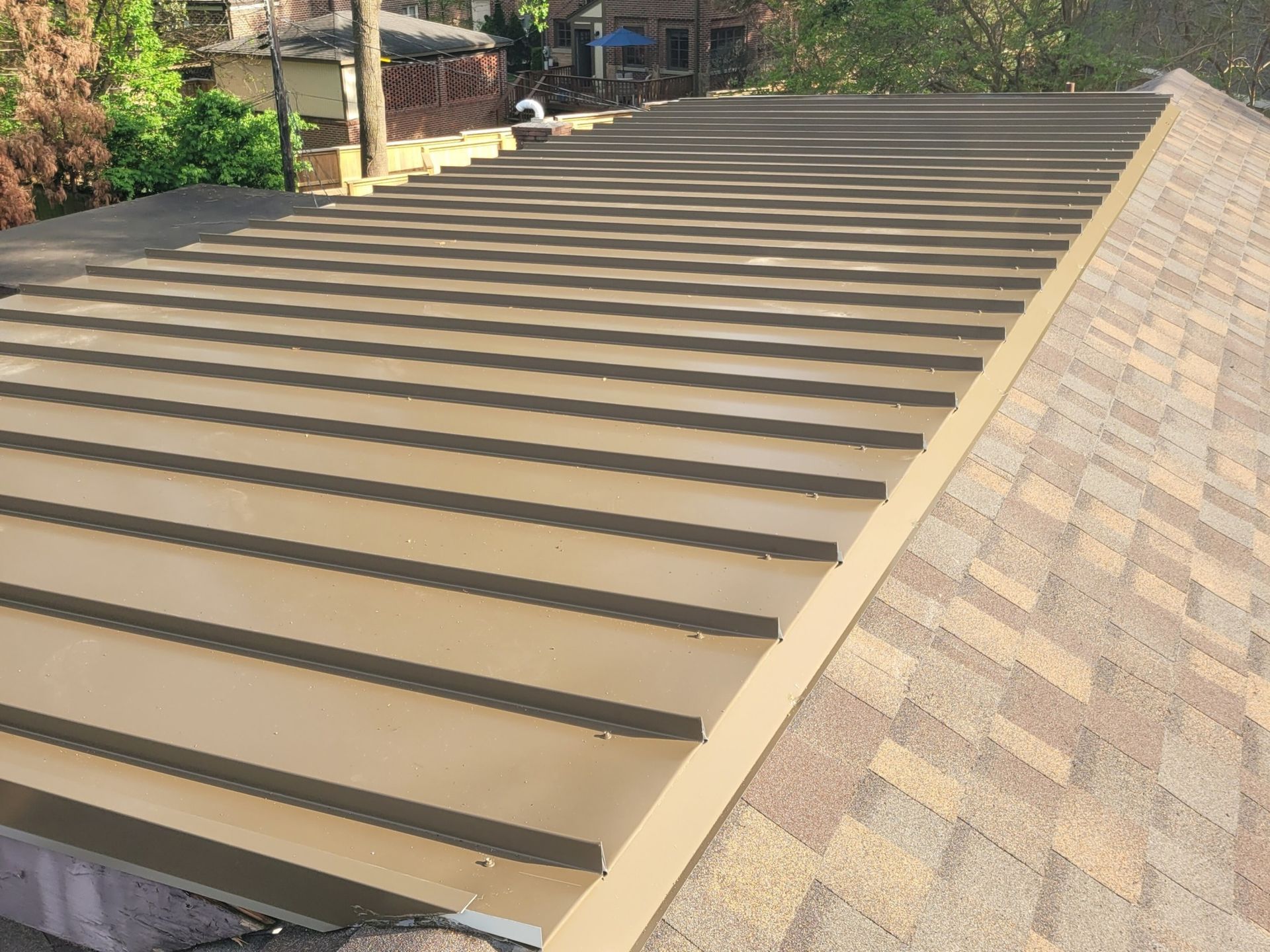 Close-up of a brown metal roof section with horizontal lines and asphalt shingles.