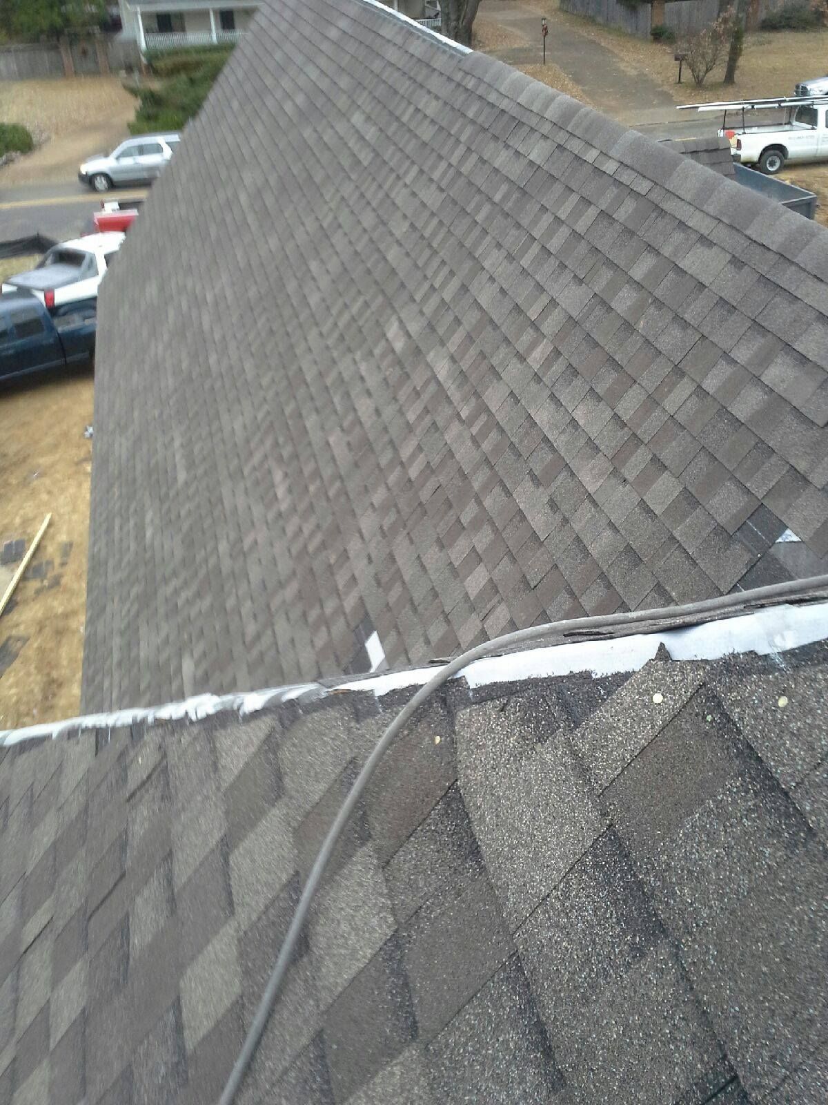 Overhead view of a shingled roof on a house with a dark cable running across the shingles.