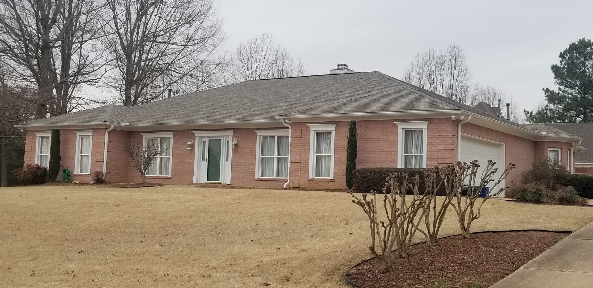 Brick house with gray roof, white trim, and brown yard. Bare trees and overcast sky.