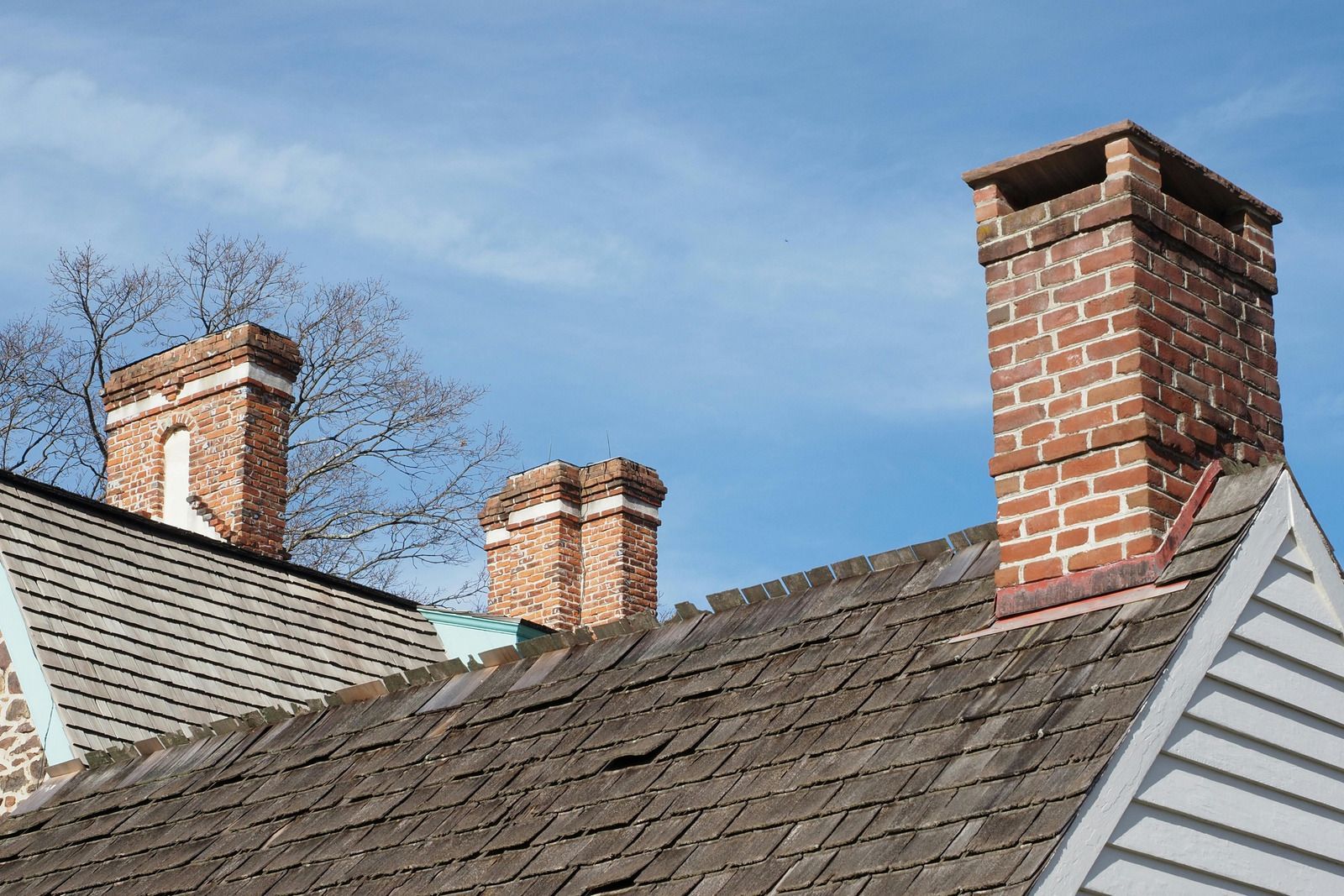 Brick chimneys on a weathered wood shingle roof against a blue sky.