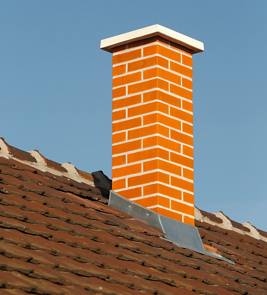 Brick chimney on a tiled roof against a blue sky