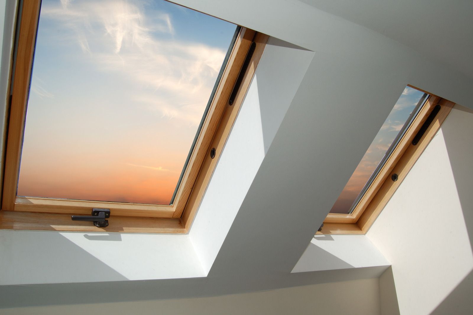 Two skylight windows set in a slanted white ceiling, showing a pastel sunset sky.