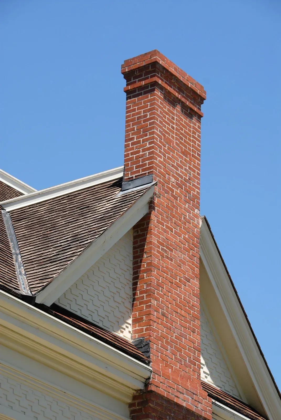 Brick chimney rising beside a house roof against a blue sky
