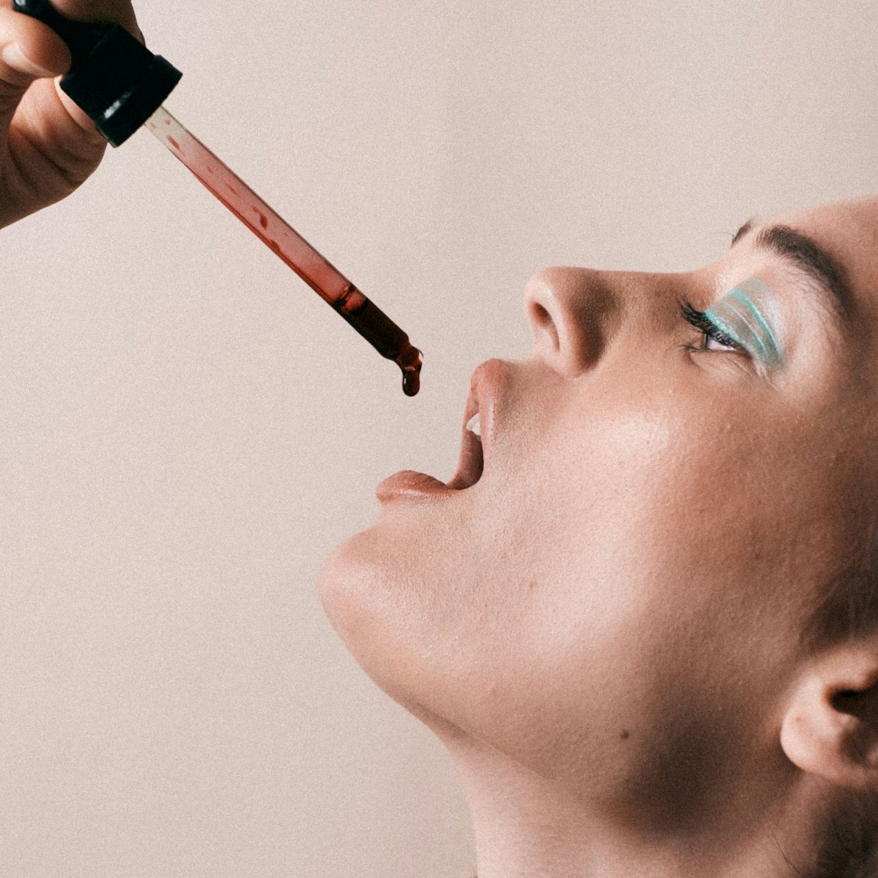 Woman applying liquid lip gloss with a wand, close-up side profile against a plain background