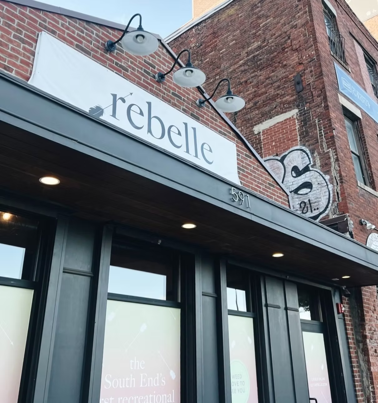 Storefront with the sign “rebelle” on a brick building, with an outdoor light fixture above.
