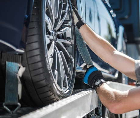 Roadside assistance professional securing a disabled vehicle on a flatbed truck.
