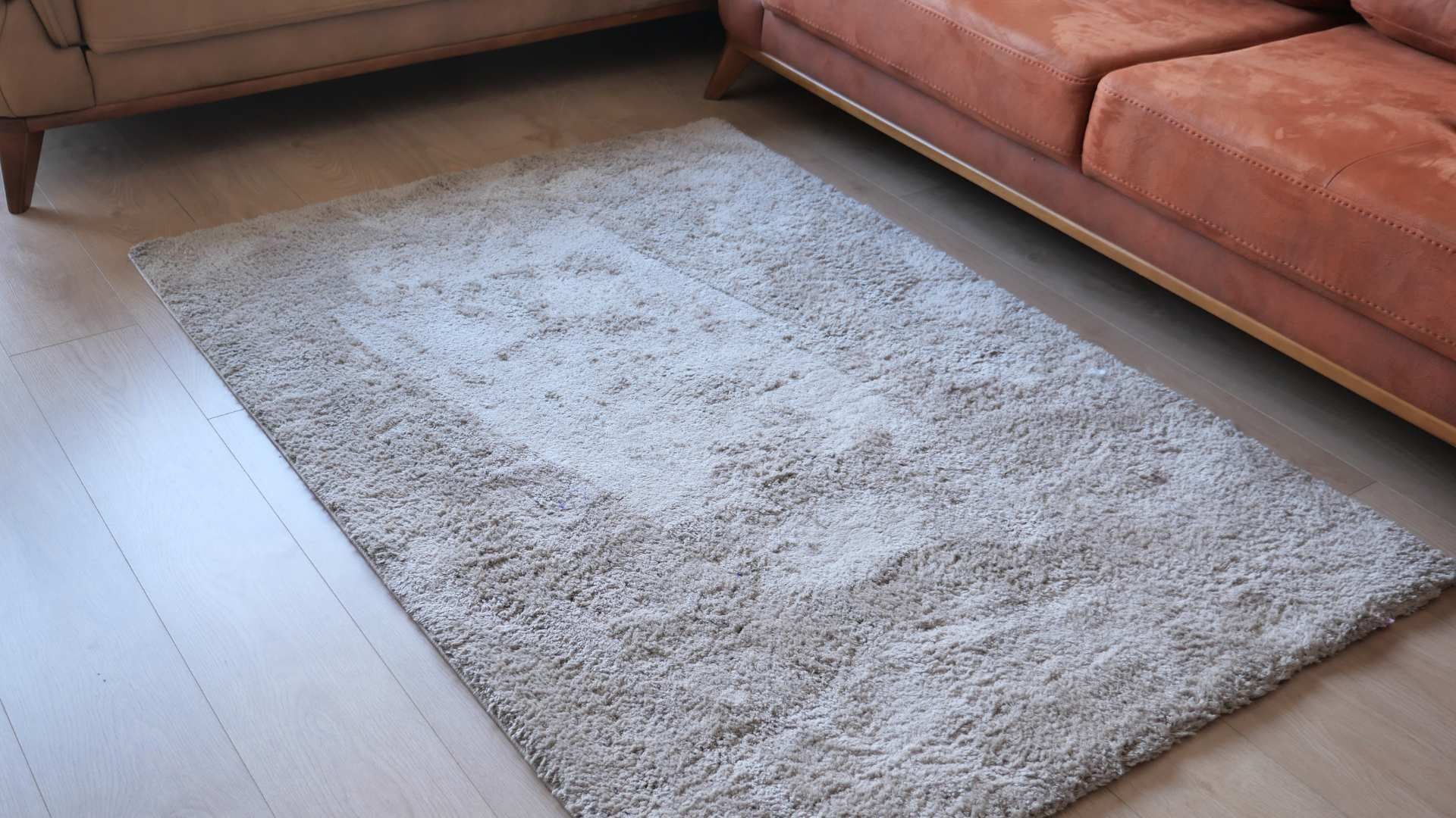 Light gray rug on a wooden floor beside a brown sofa.