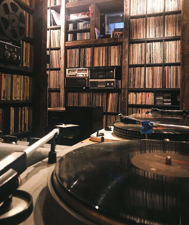 Turntables in a cozy room lined with shelves of vinyl records and books.