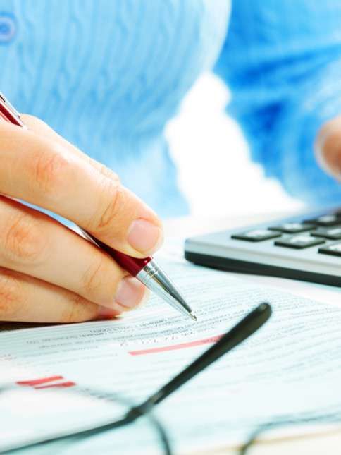 Hand writing on a form with a pen beside a calculator