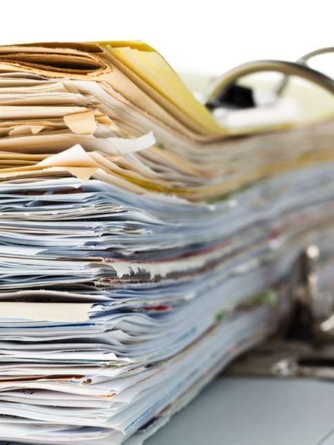Stack of assorted paper files and folders piled high on a desk