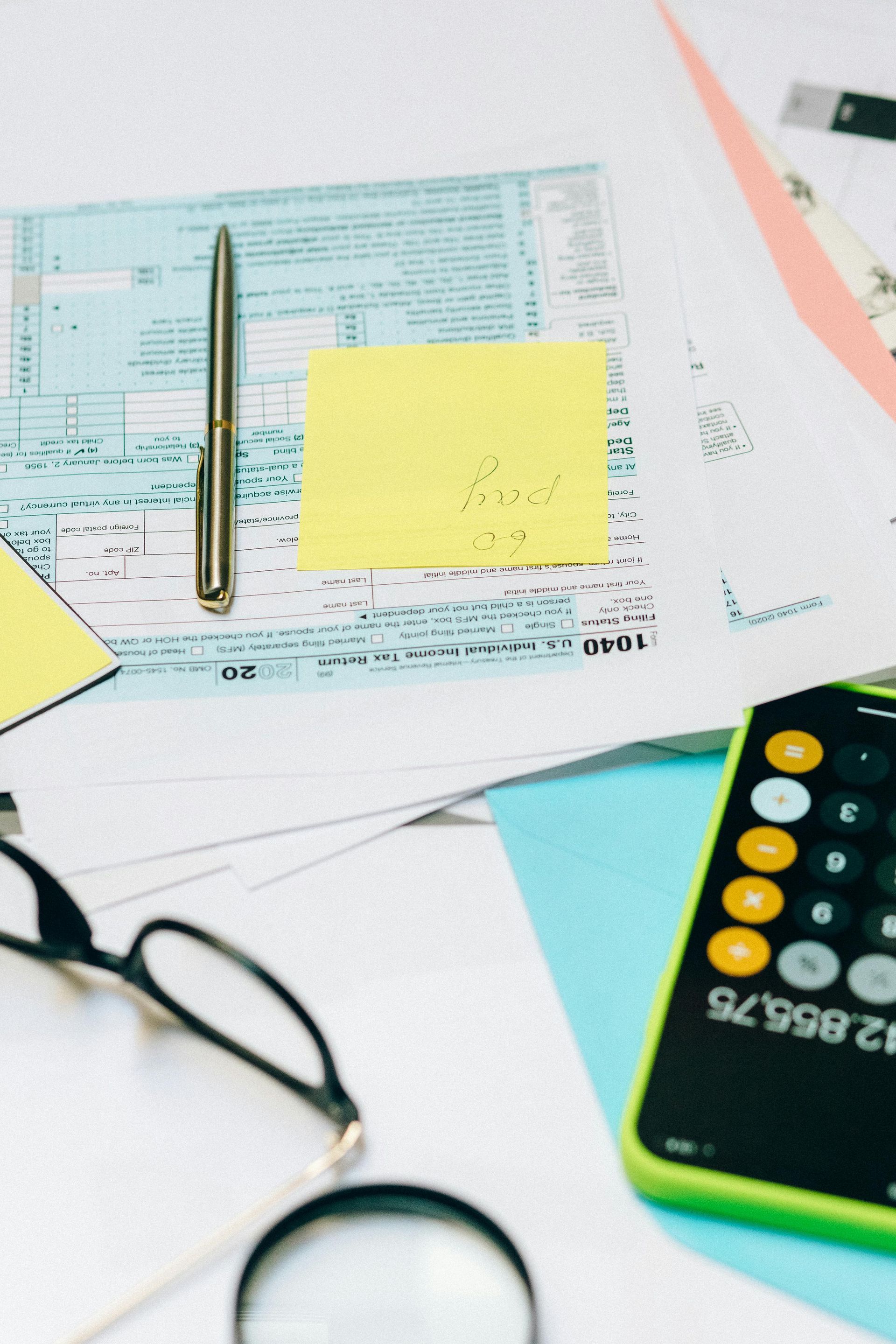 Office desk with tax forms, pen, calculator, sticky note, and glasses
