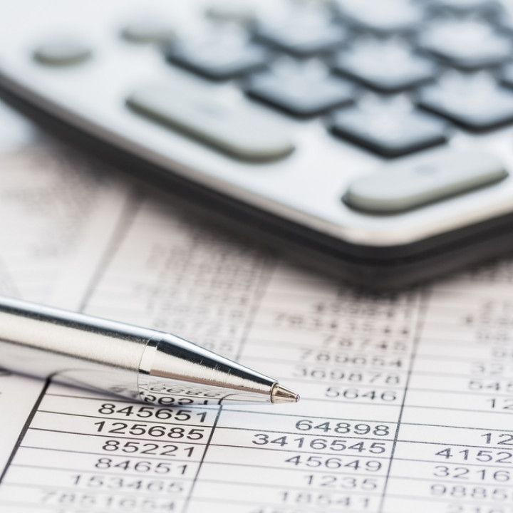Calculator and pen over financial ledger with numbers and a keyboard in the background