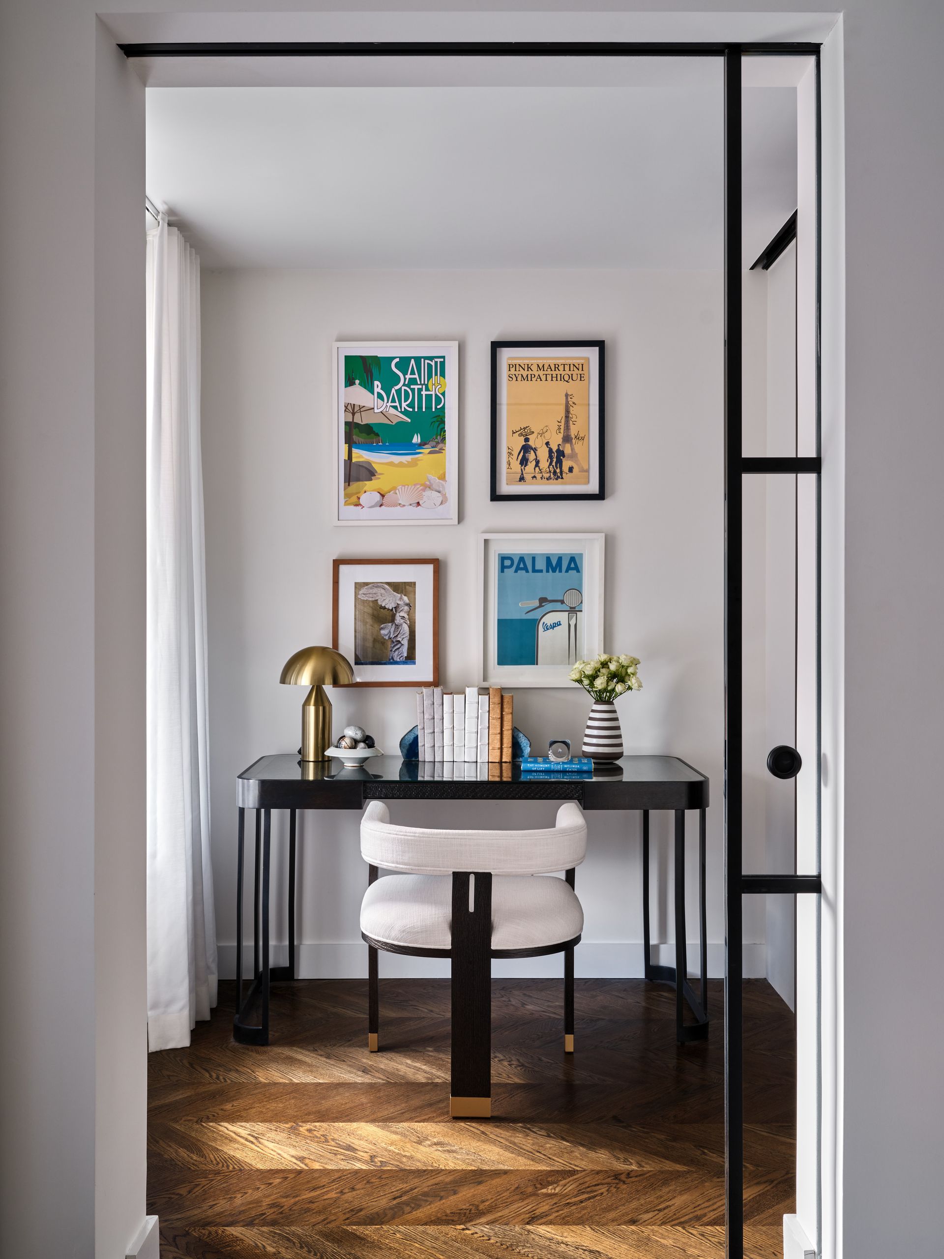Small home office nook with a black desk, white chair, framed art, and plants in a doorway alcove.