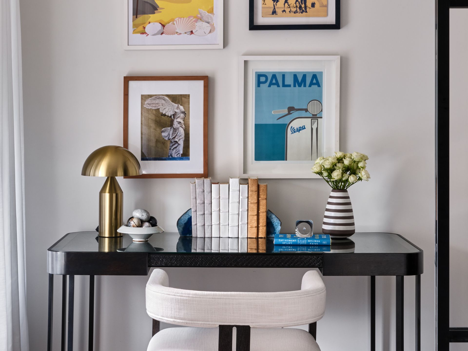 Stylish home desk with black table, books, lamp, flowers, and framed wall art