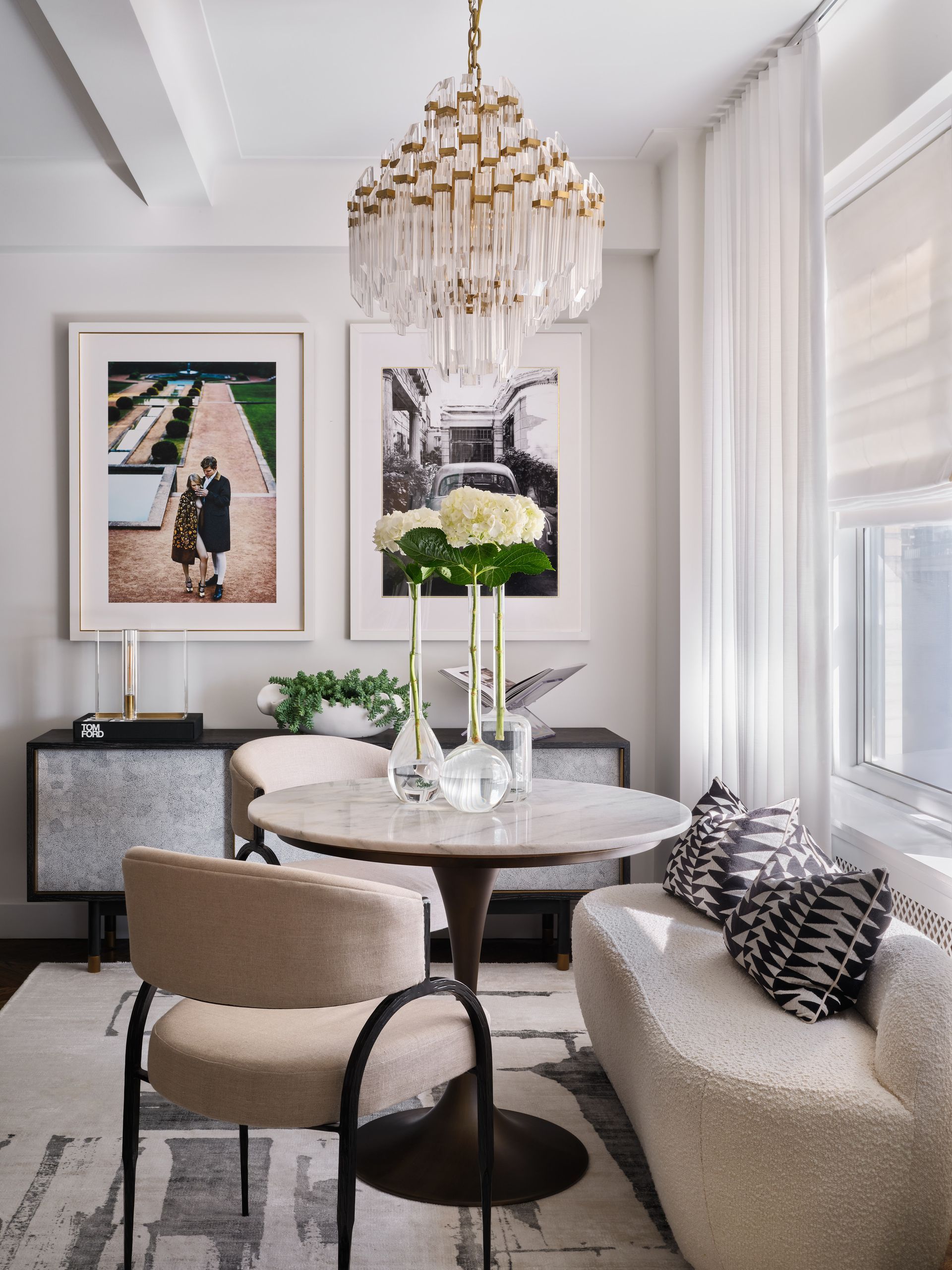 Elegant dining nook with chandelier, round marble table, beige chairs, and large windows with sheer curtains