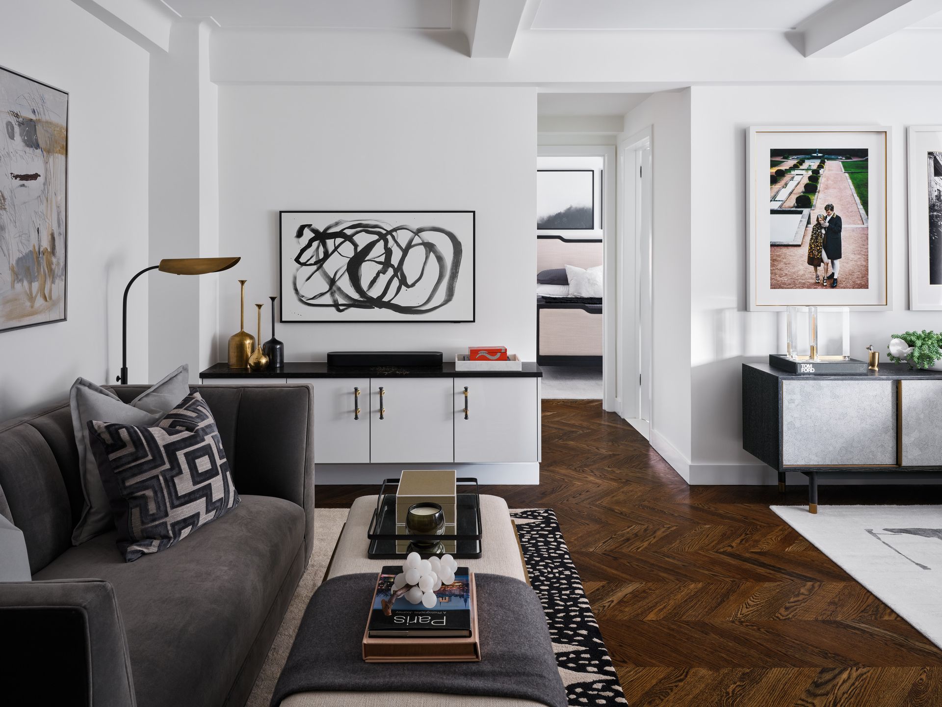 Modern living room with gray sofa, black-and-white art, and herringbone wood floor.