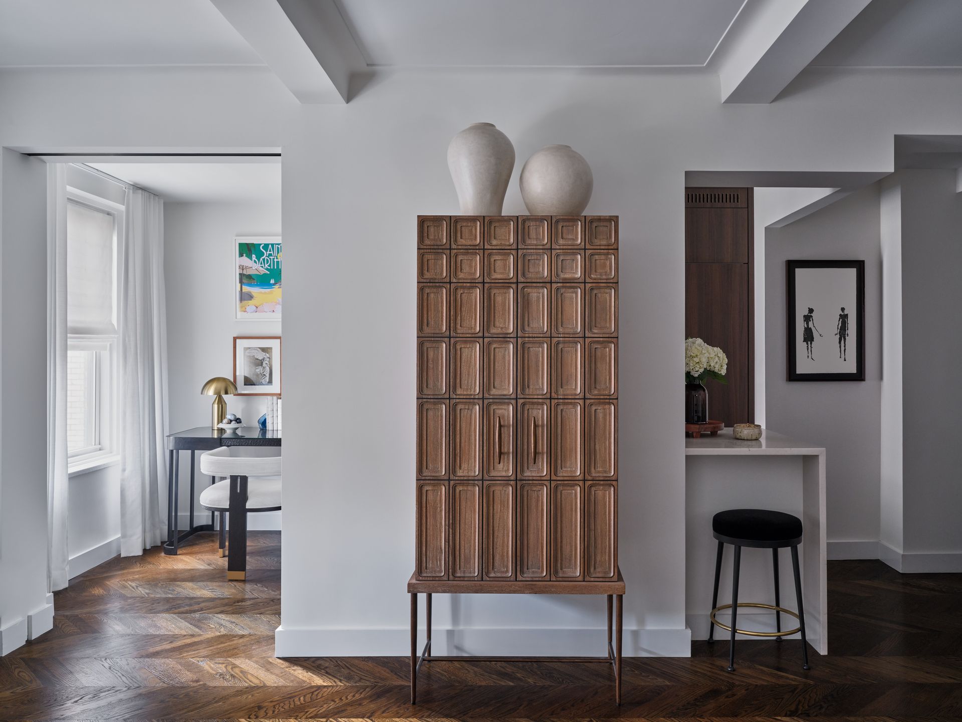 Modern living space with a tall wooden cabinet, white walls, and a small desk in the background