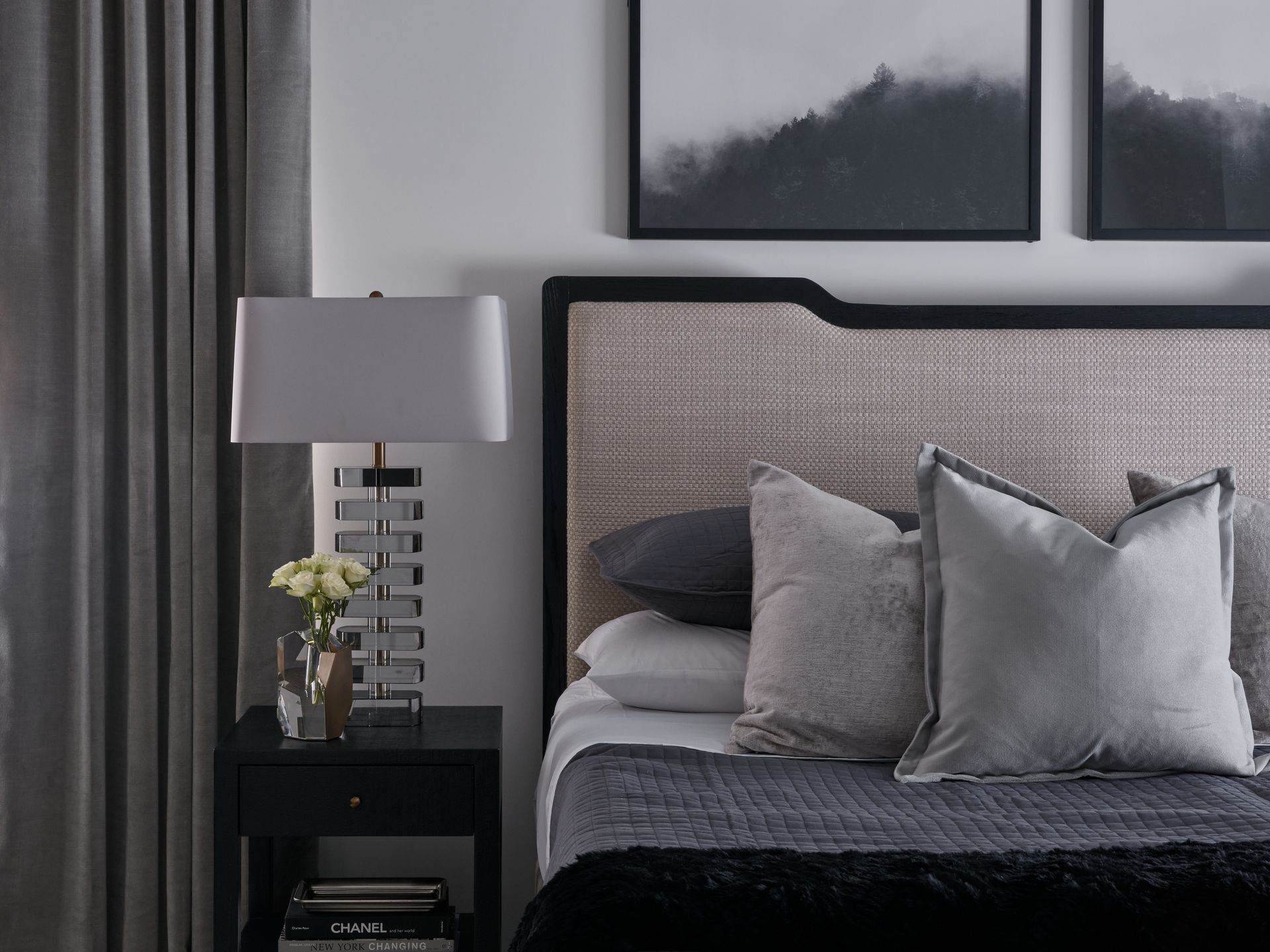 Modern bedroom with a gray upholstered bed, bedside lamp, and dark curtains