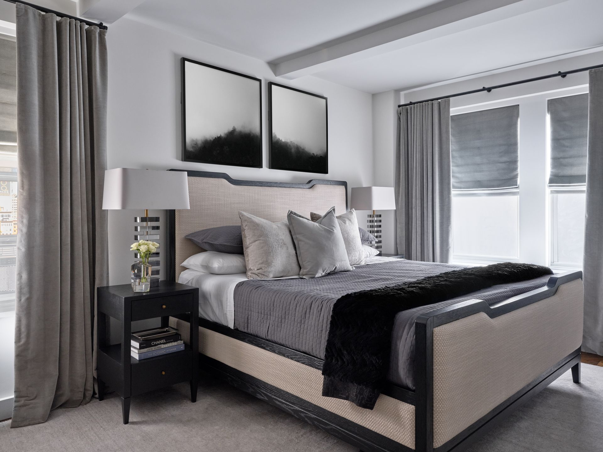 Bright modern bedroom with a gray bed, black lamps, and large windows with blinds.