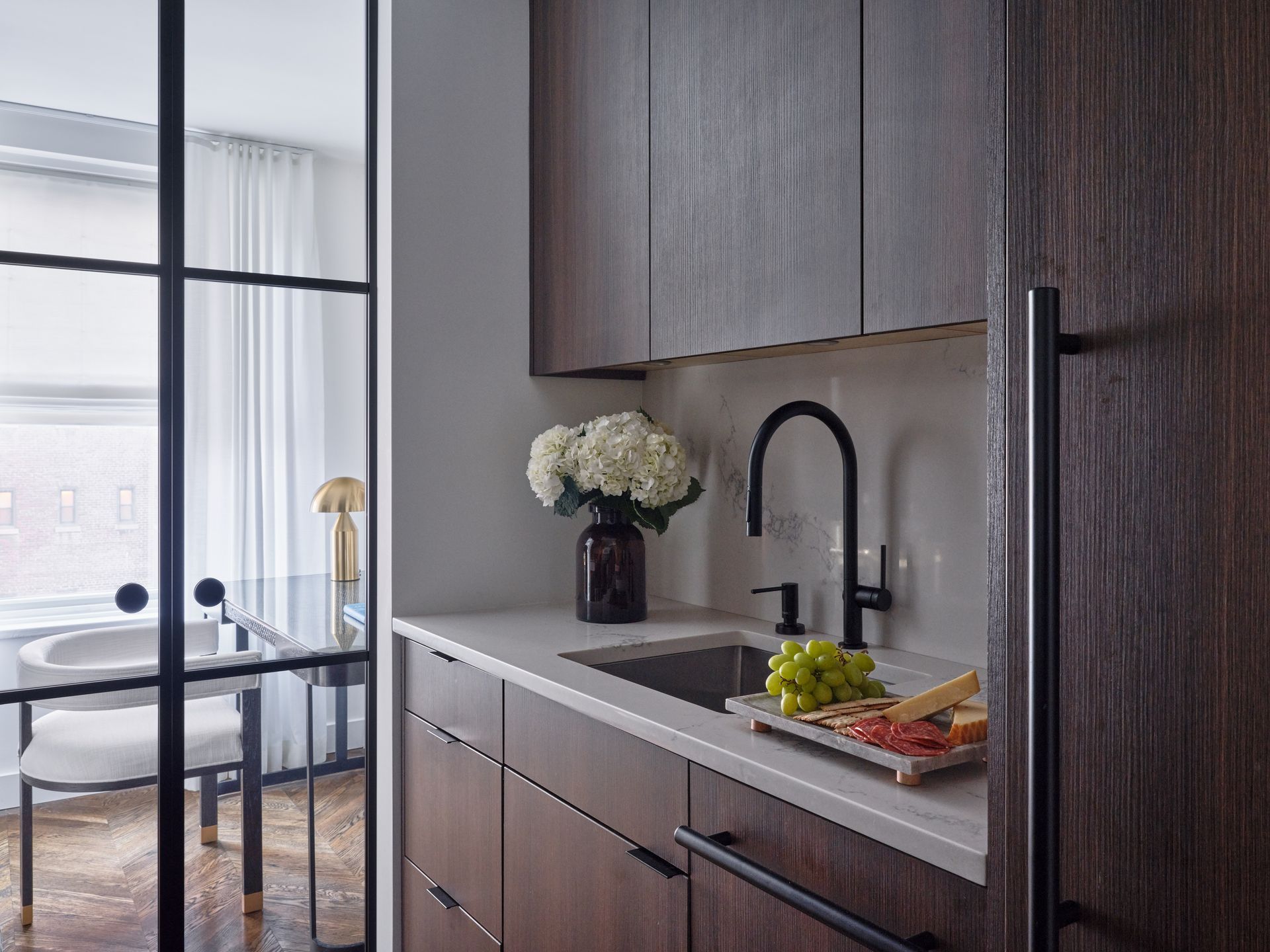 Modern kitchen with dark wood cabinets, sink, flowers, and a plate of fruit by a bright window